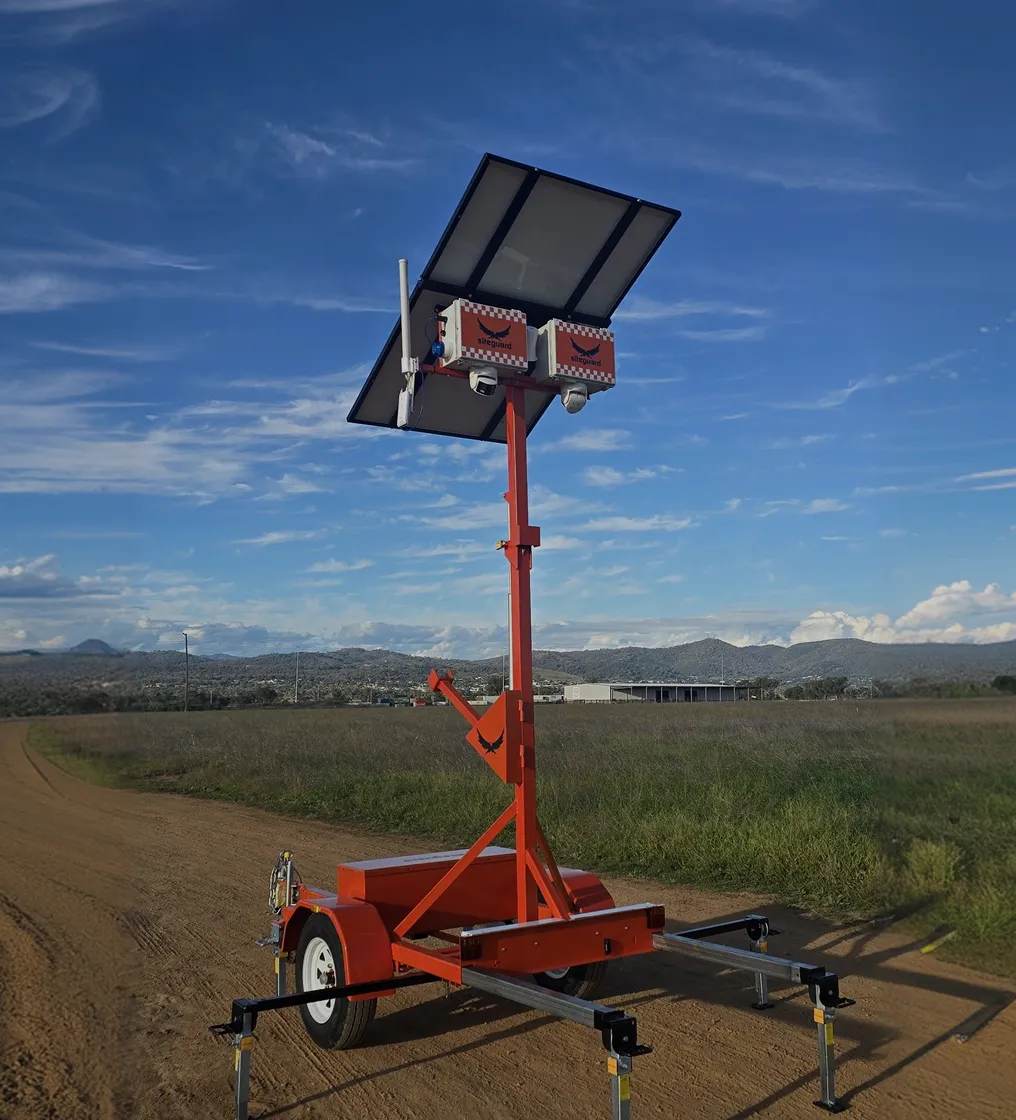 Mobile solar-powered site security camera unit with two cameras on a dirt road in a rural setting.