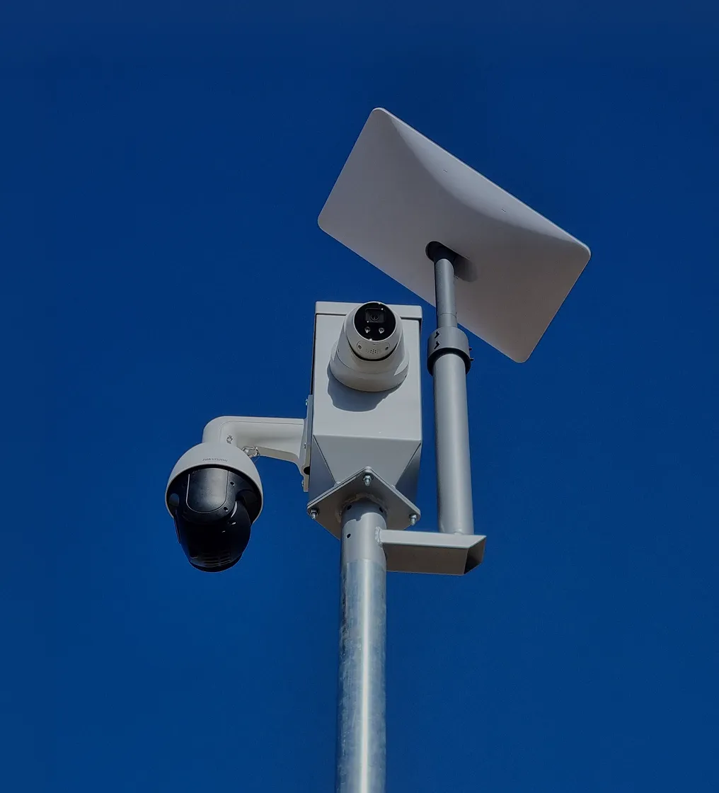 Two white security cameras mounted on a metal pole with a solar panel against a clear blue sky.
