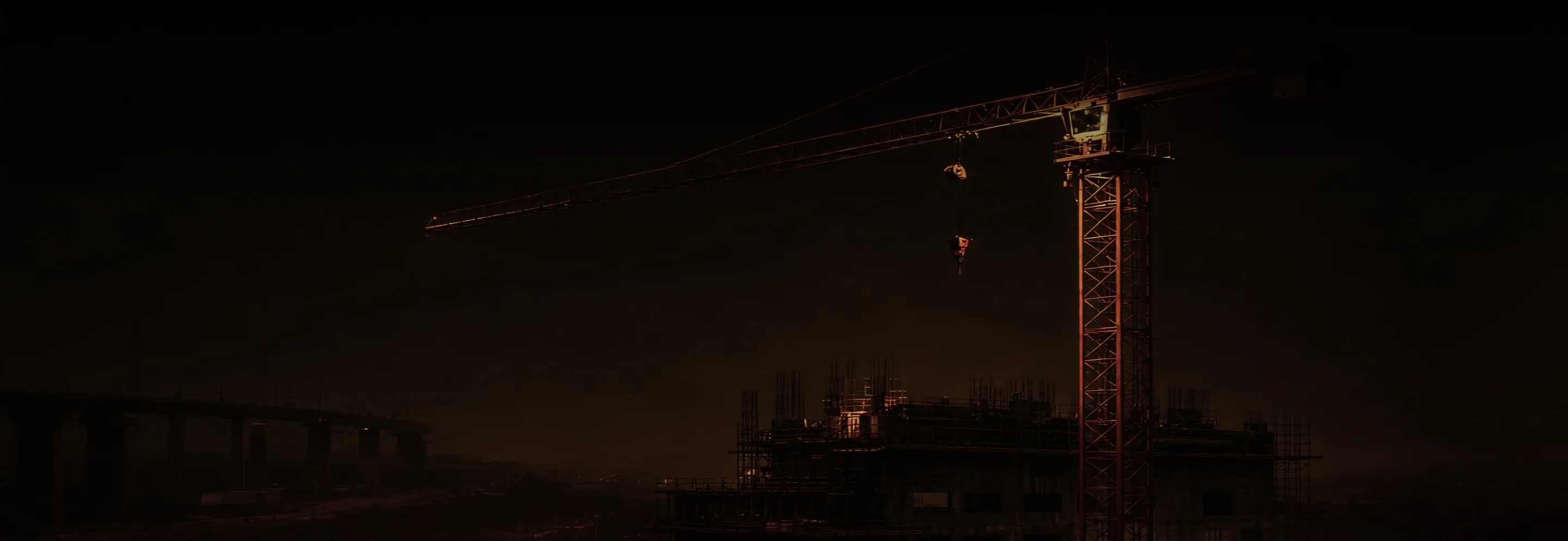 Construction crane illuminated at night above an unfinished building with a dark sky background.