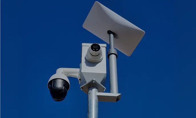 Security camera mounted on a metal pole against a clear blue sky.