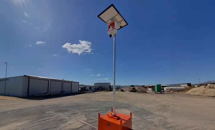 Solar-powered security camera mounted on a tall pole in an industrial yard under a clear blue sky.