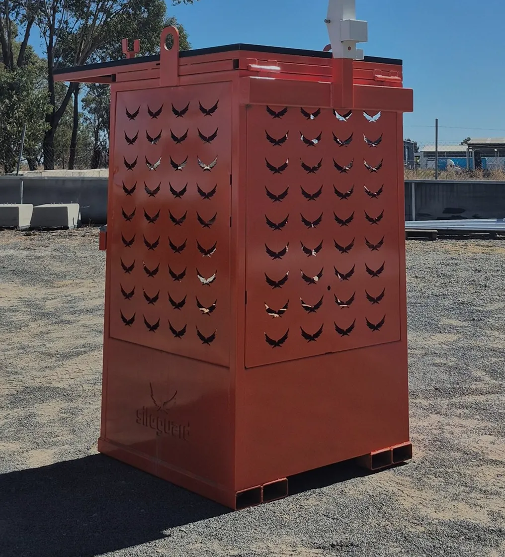Tall orange metal enclosure with bird-shaped ventilation cutouts standing on gravel outdoors.