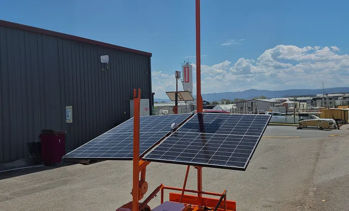 Orange Siteguard solar CCTV trailer with twin solar panels and a raised mast in an industrial yard