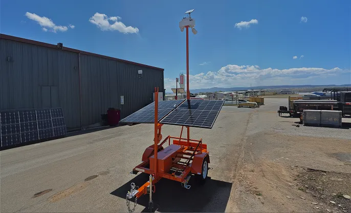 Orange mobile solar panel system mounted on a small trailer in an industrial outdoor area.