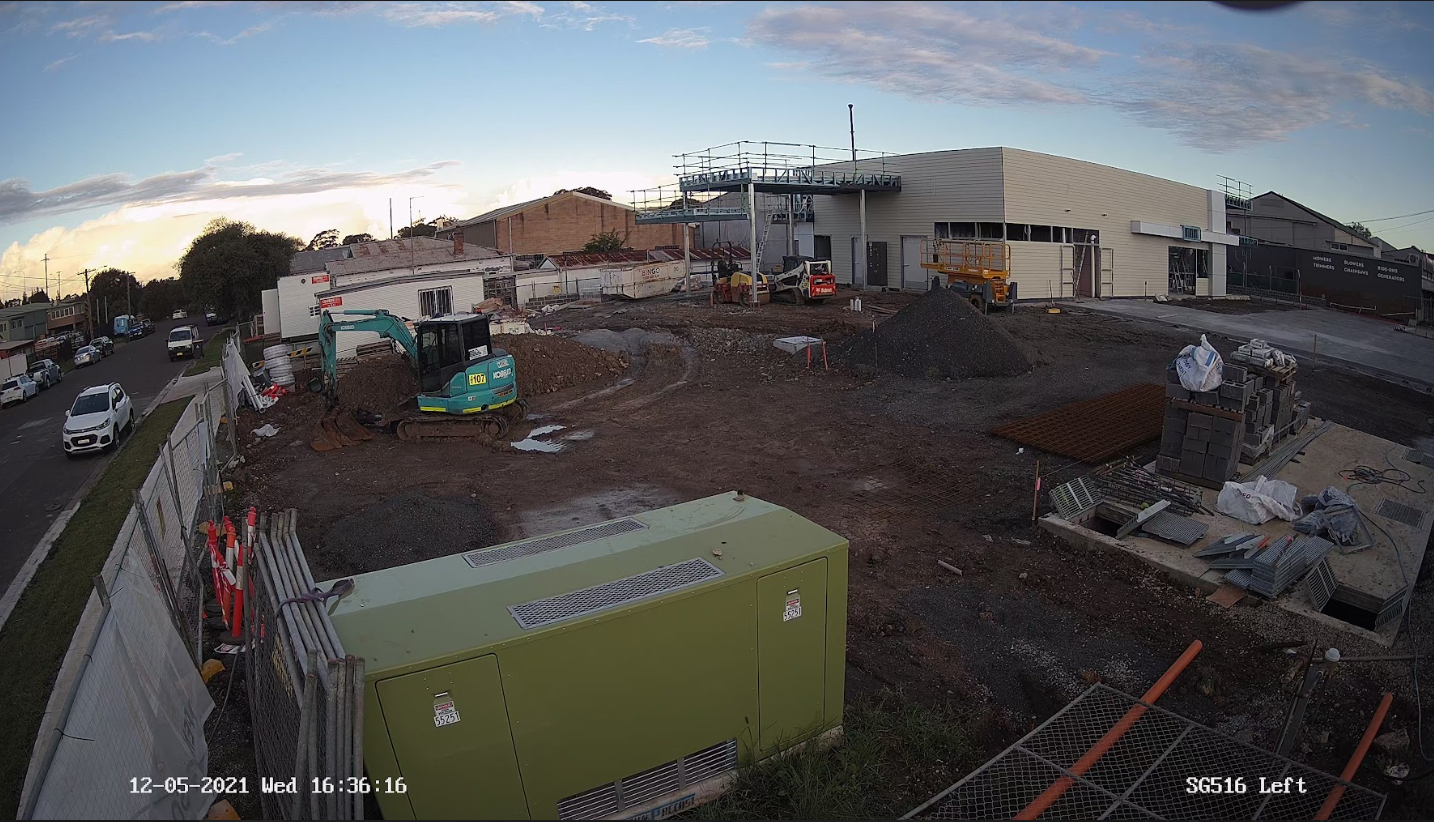 Timestamped security camera view of a construction site with an excavator, generator, temporary fencing and stacked materials