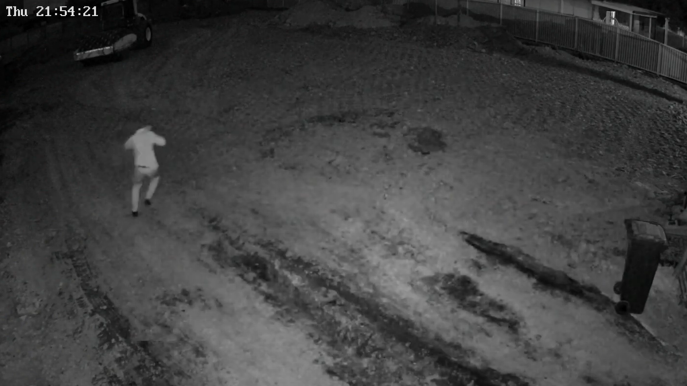 Night-vision site camera footage of a person crossing an empty block at 9:54pm