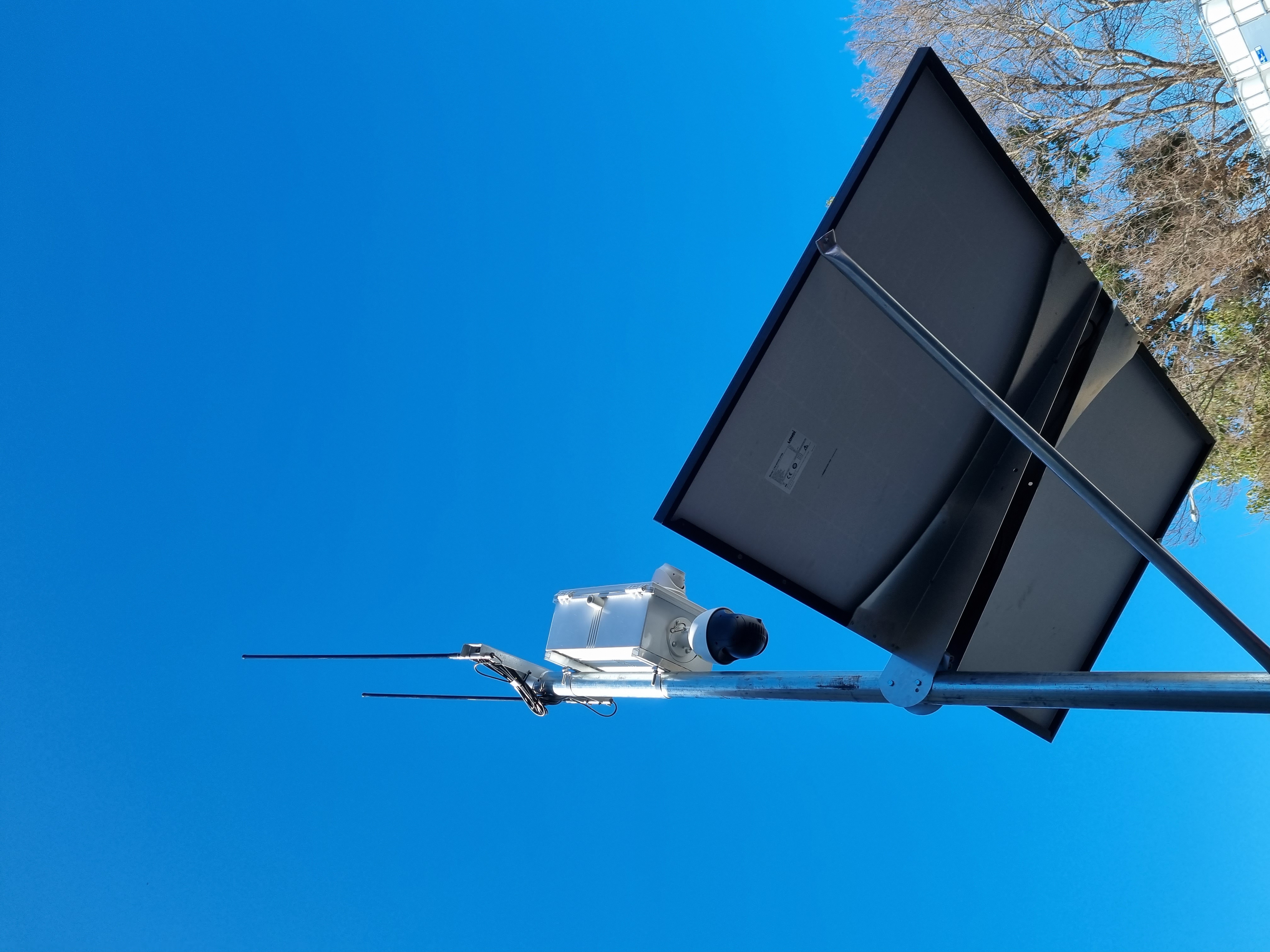 Siteguard PTZ camera with two antennas mounted on a pole above a solar panel, against a clear blue sky