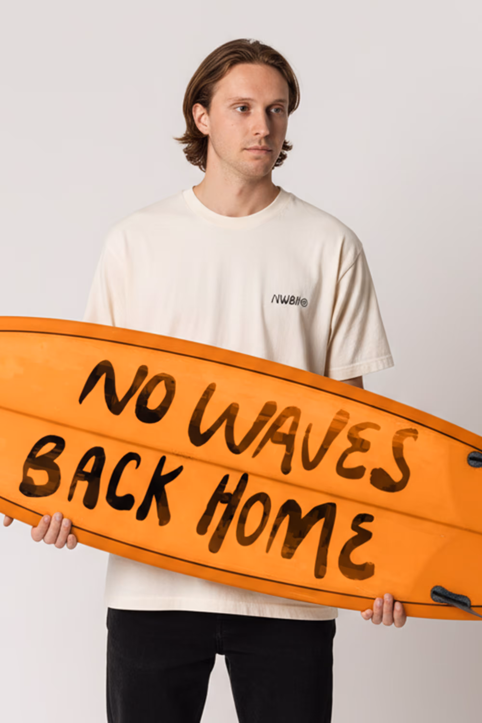 Man in white shirt holding an orange surfboard with text 'NO WAVES BACK HOME'.