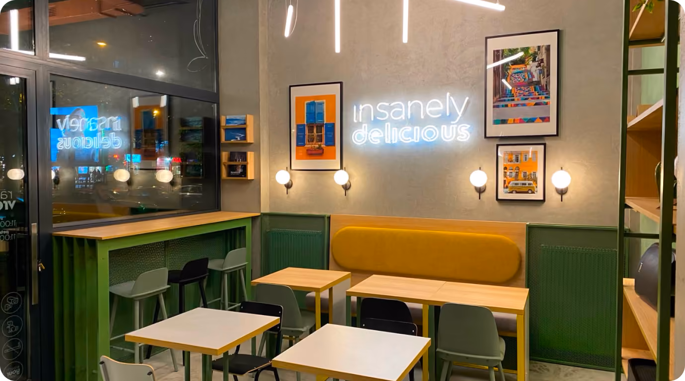 Moderno kafić sa zelenim detaljima, žutom klupom, stolovima i natpisom neon svetlom 'insanely delicious'.