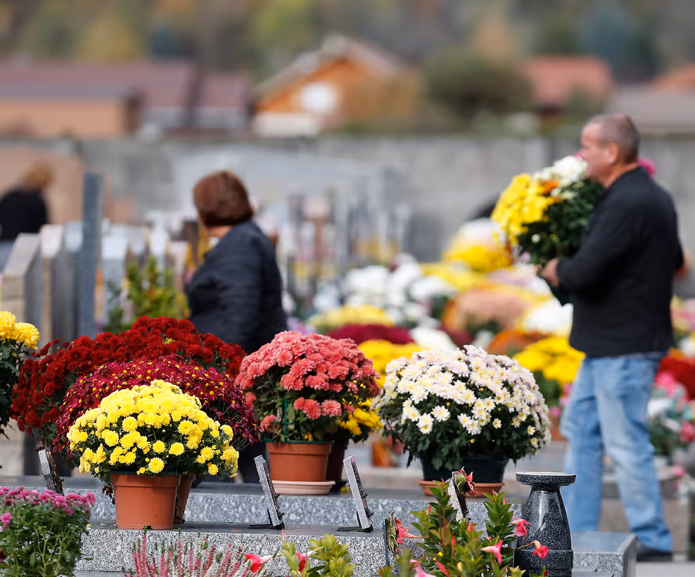 Ľudia držia kytice a stoja pri hroboch s kvetmi na cintoríne na jeseň.