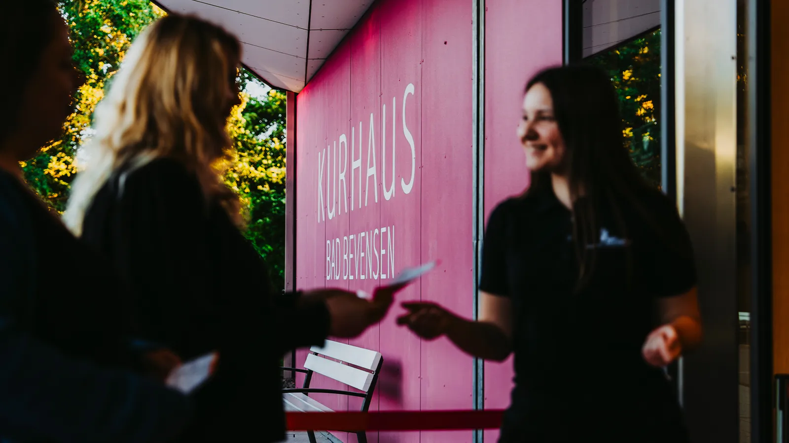 Freundliche Begrüßung durch eine Mitarbeiterin vor der markanten rosa Fassade des Kurhauses Bad Bevensen zum Start Ihrer Eventanfrage.