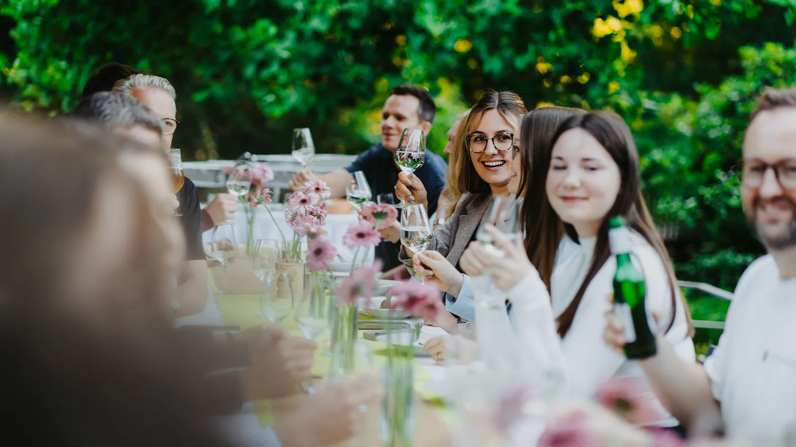 Glückliche Gäste stoßen bei der erfolgreichen Realisierung eines Events an einer festlich gedeckten Tafel auf der sonnigen Kurterrasse an.