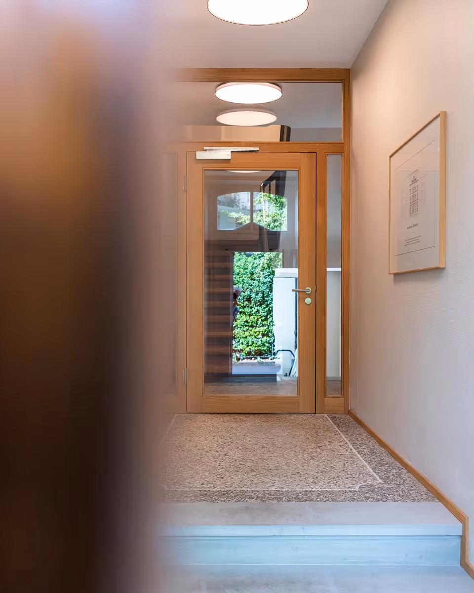 Eingang mit Holztür und Glasfenster, Flur mit Teppich und beleuchteter Deckenlampe.