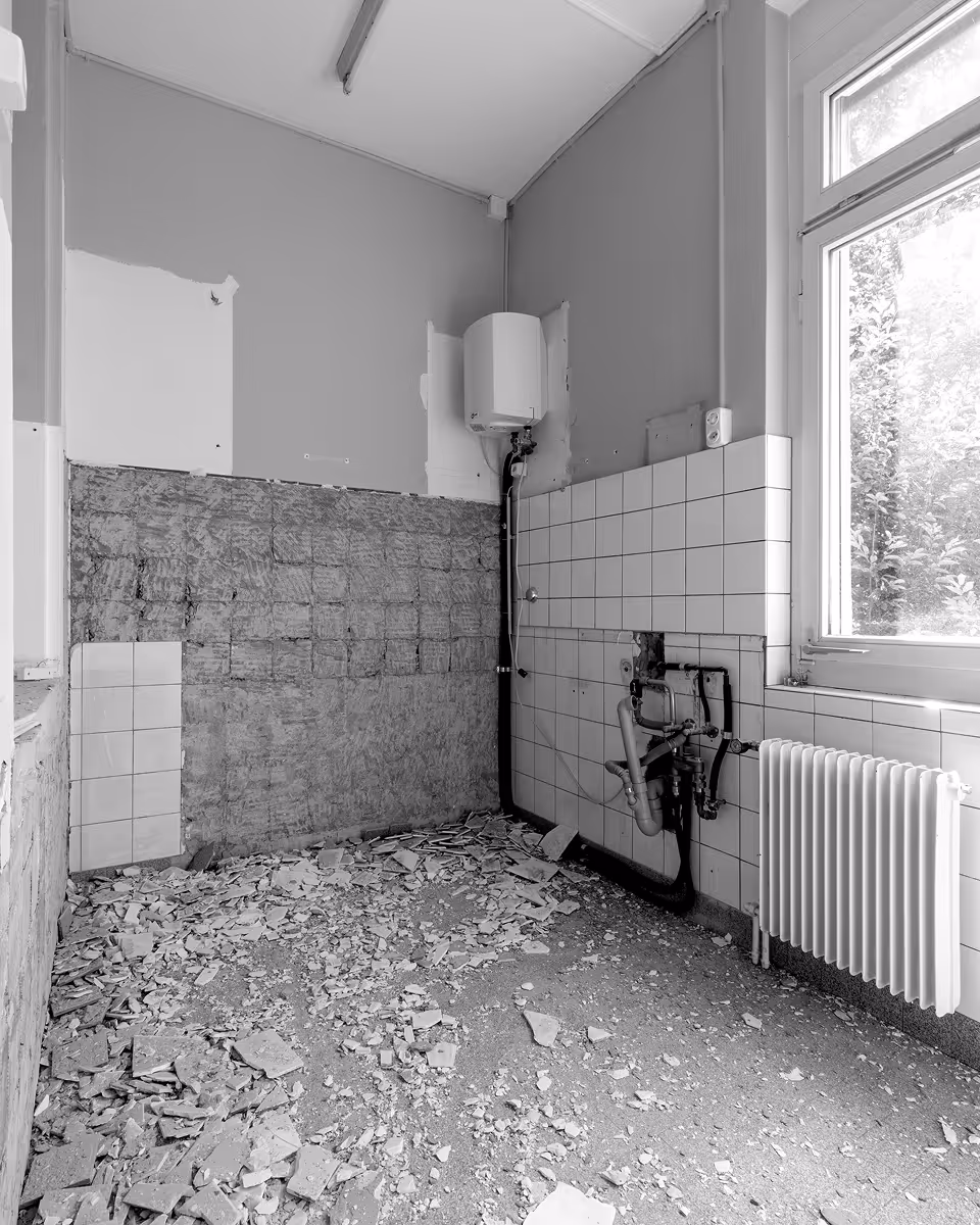 Renoviertes Zimmer mit entferntem Wandbelag, freiliegenden Rohren und Heizung unter Fenster.