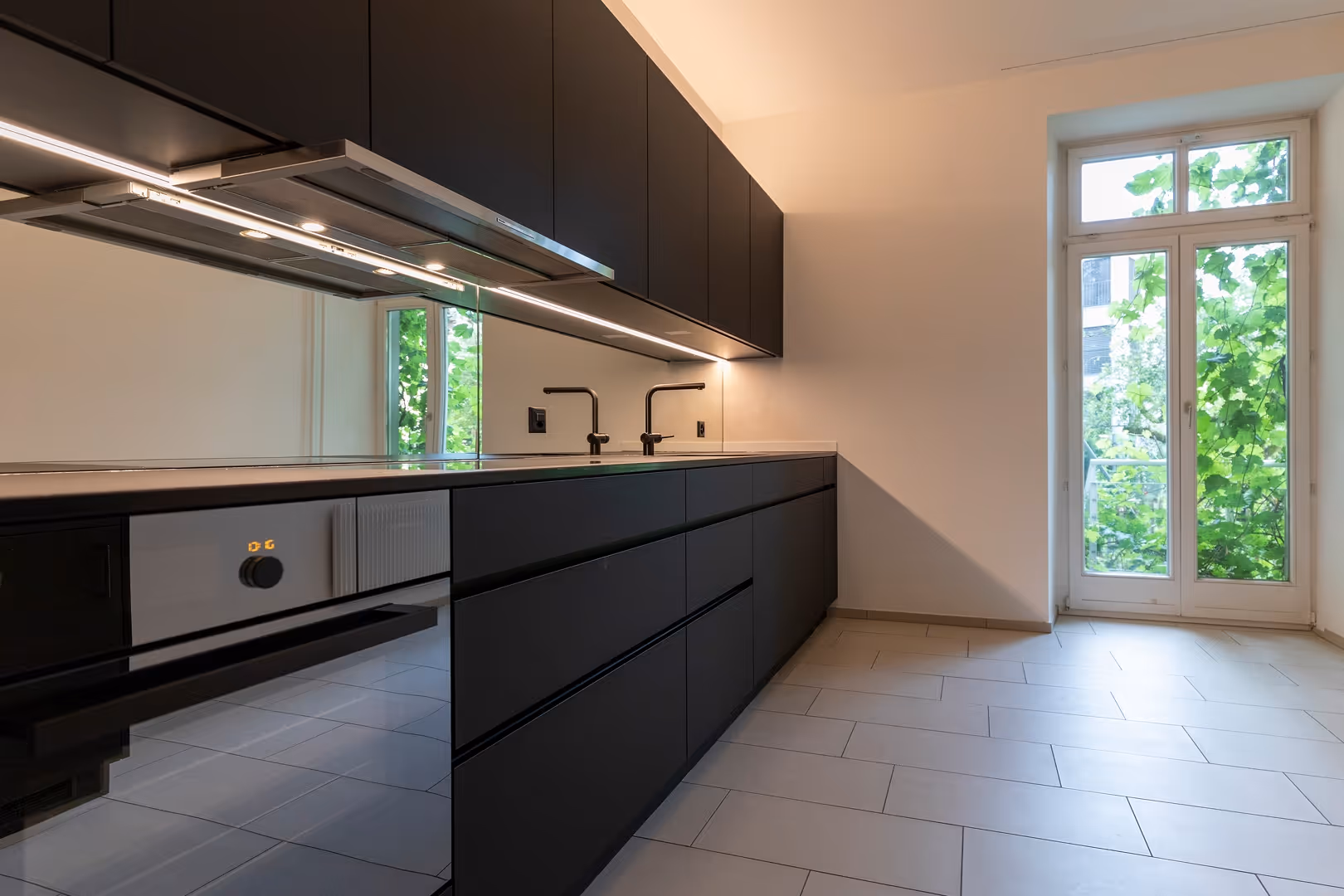 Moderne Küche mit schwarzen Schränken, zwei Wasserhähnen und großen Fenstern mit grünem Blick.