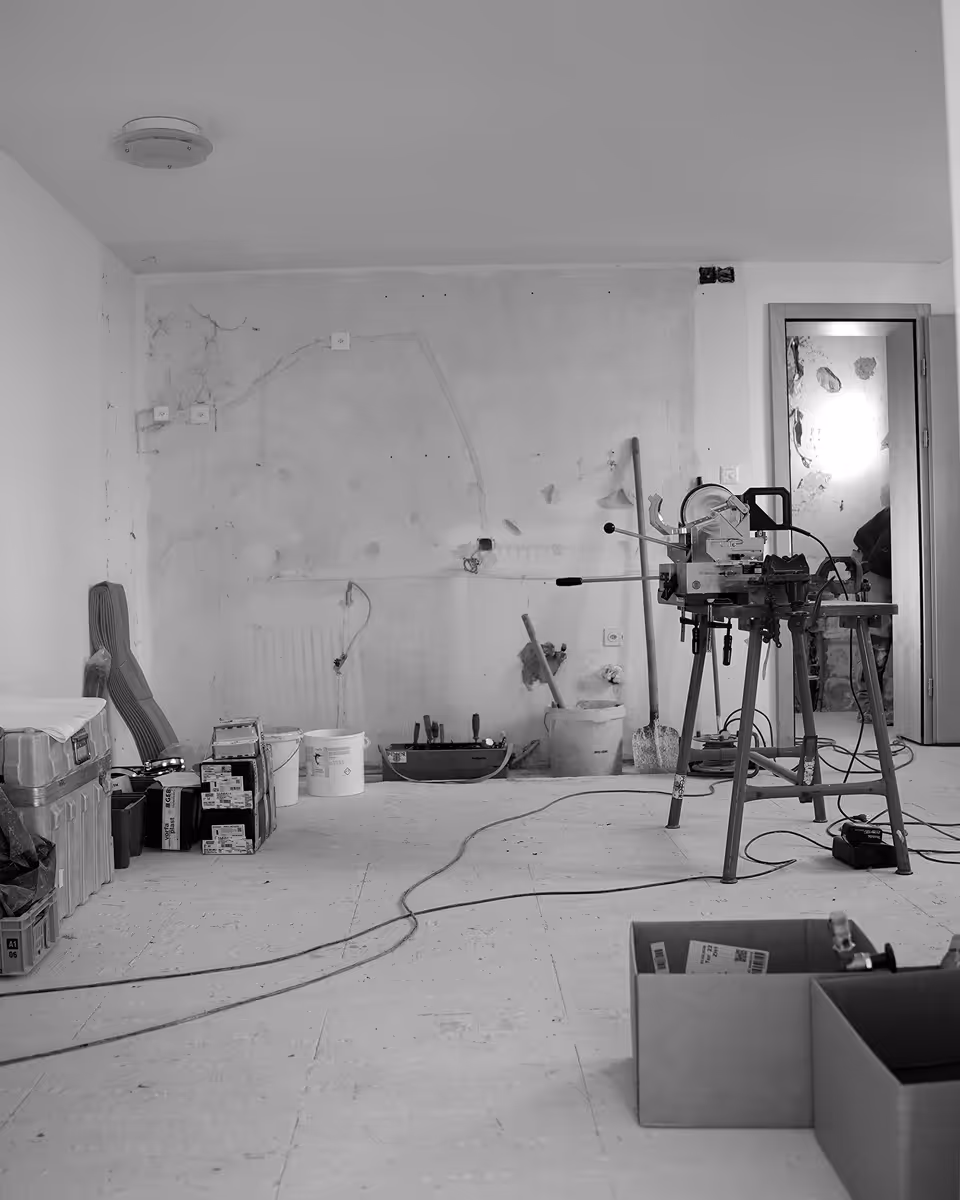 Baustelle mit Werkzeug, Eimern, Kabeln und einer Maschine auf Stativen in einem unfertigen Raum.