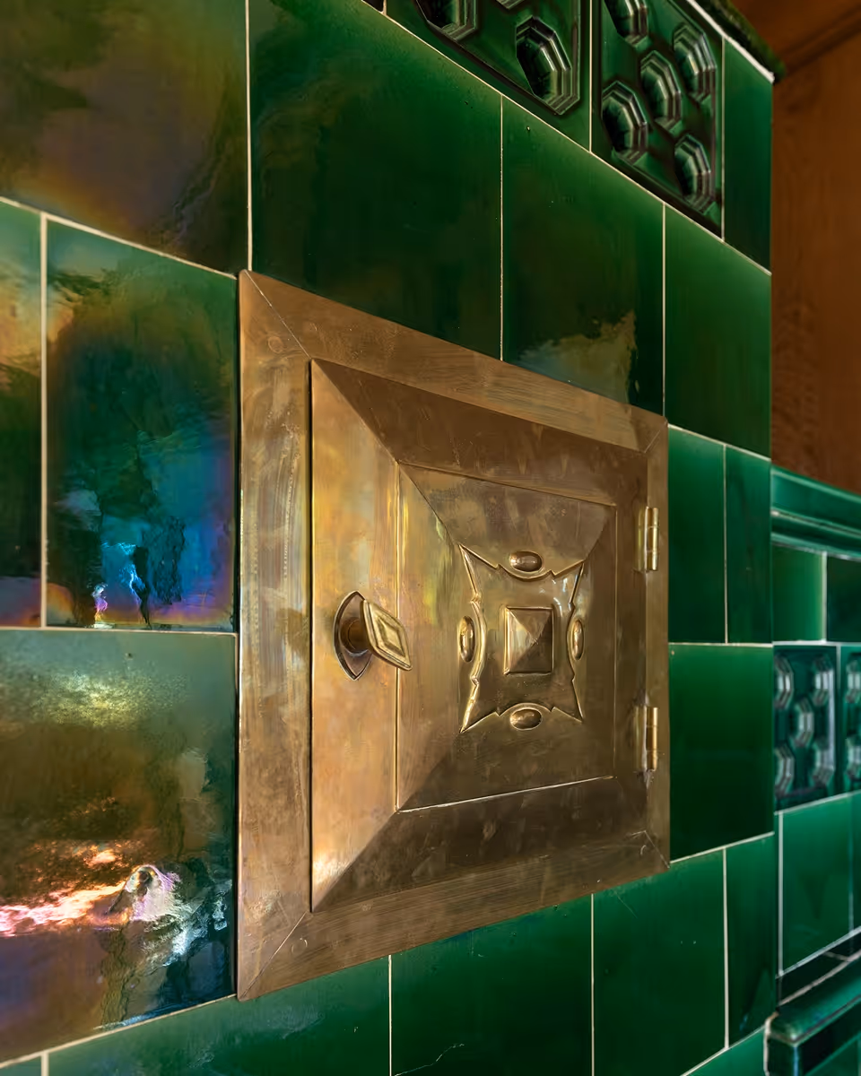 Goldfarbenes Metallfach mit Griff in grün gefliester Wand mit dekorativen Mustern.