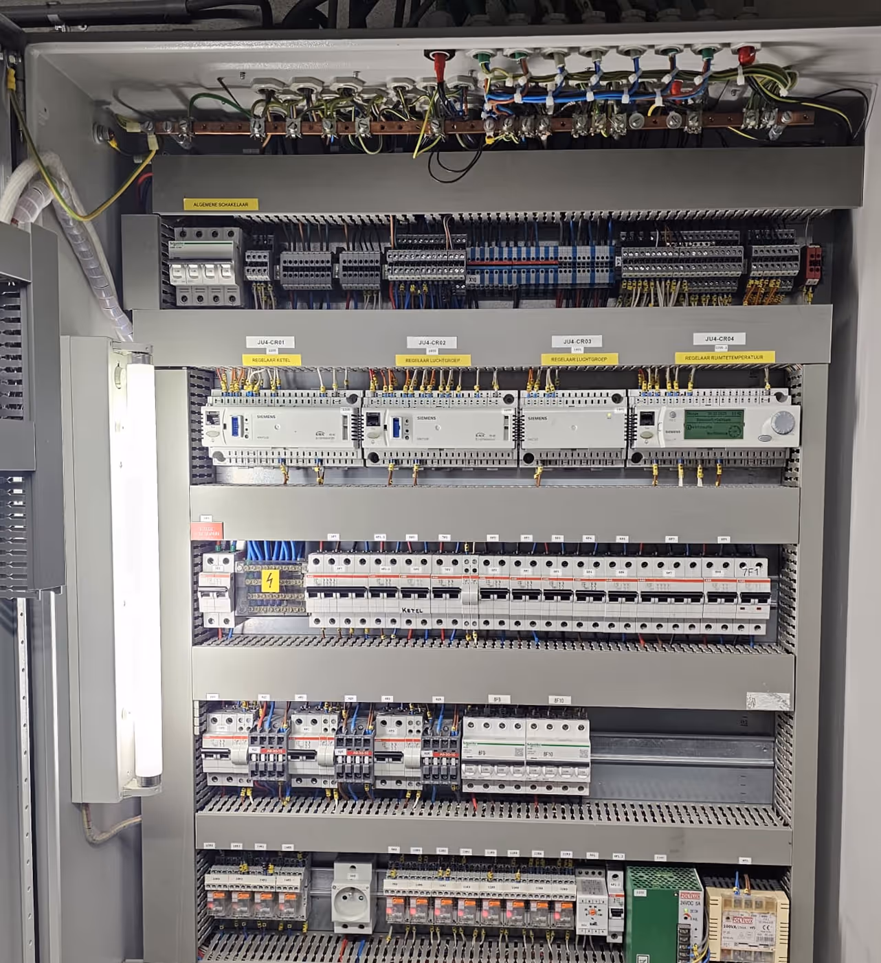 Electrical control panel with labeled Siemens modules, circuit breakers, wiring, and a mounted fluorescent light.