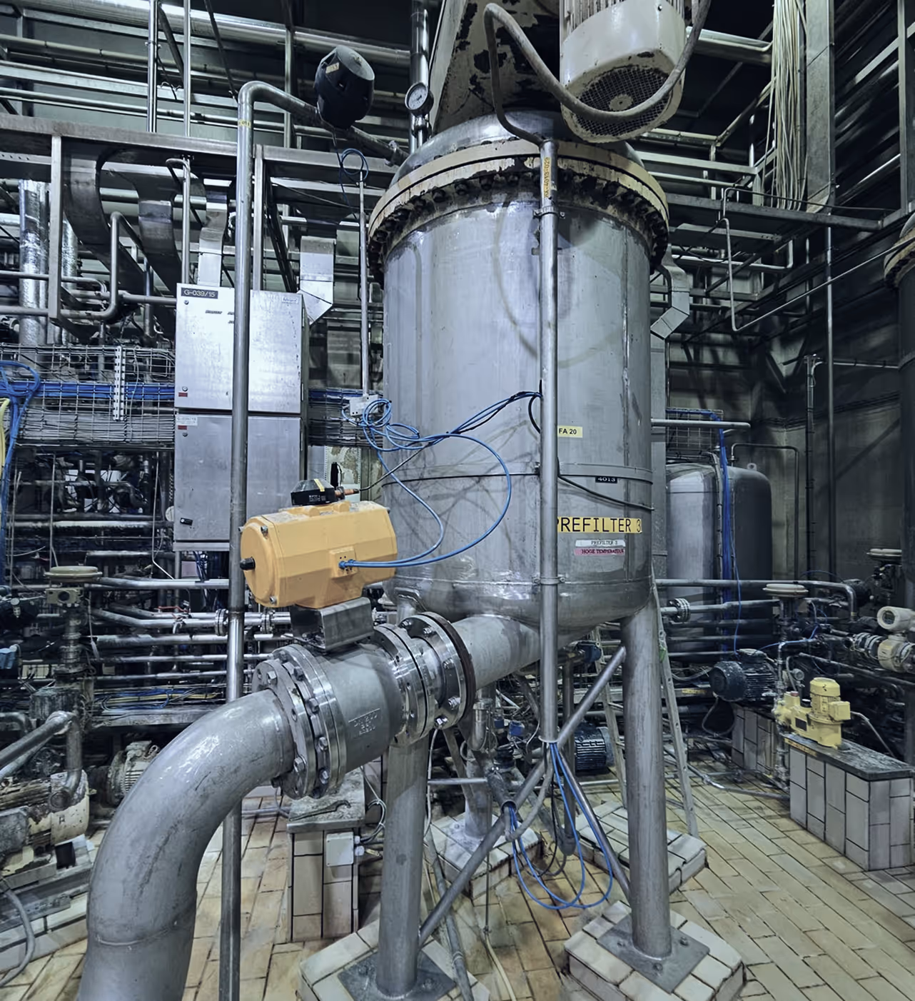 Industrial filtration system with large metal tank, pipes, and control devices in a factory setting.