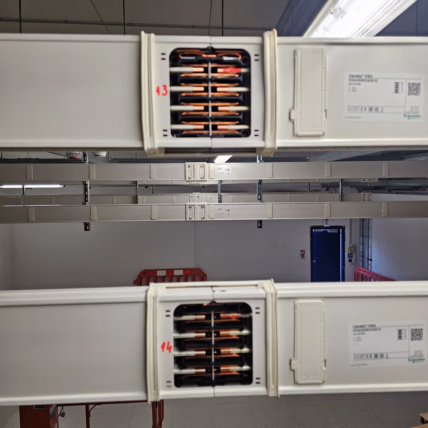Two white industrial cable trays with visible copper wiring inside in a warehouse with blue door.