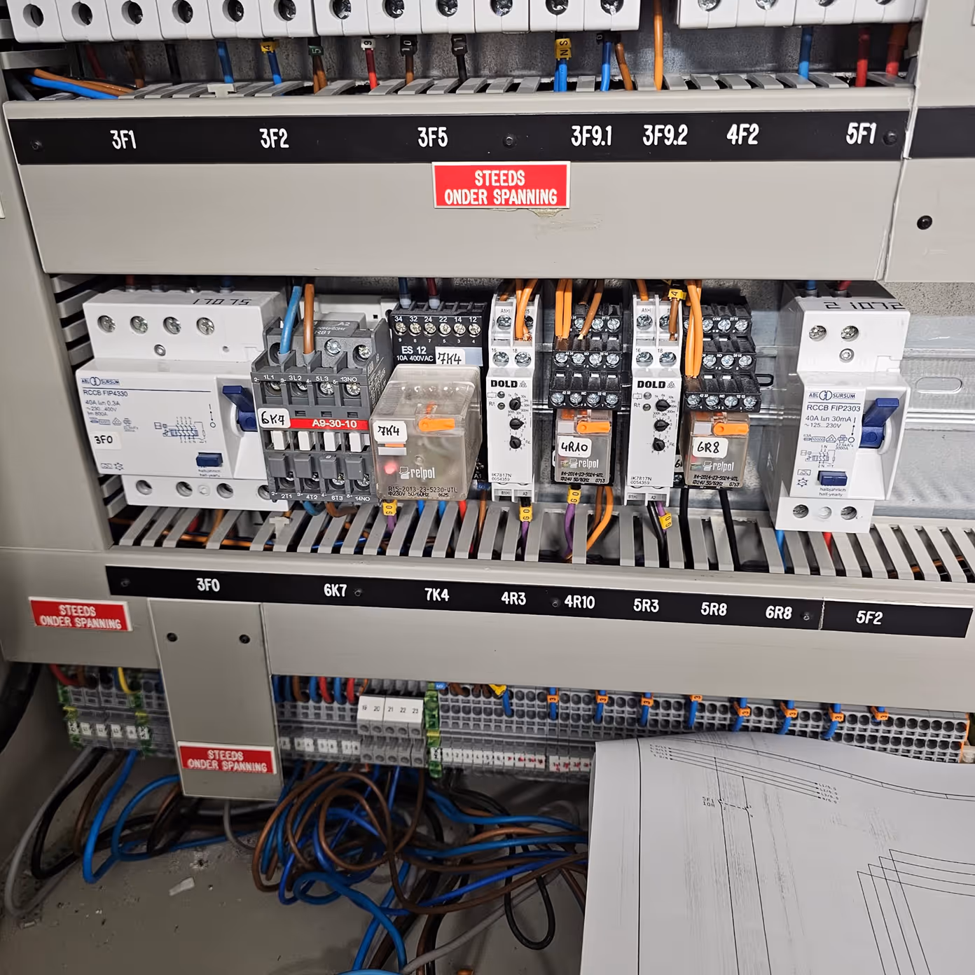 Electrical control panel with labeled circuit breakers, relays, wiring, and warning labels inside.