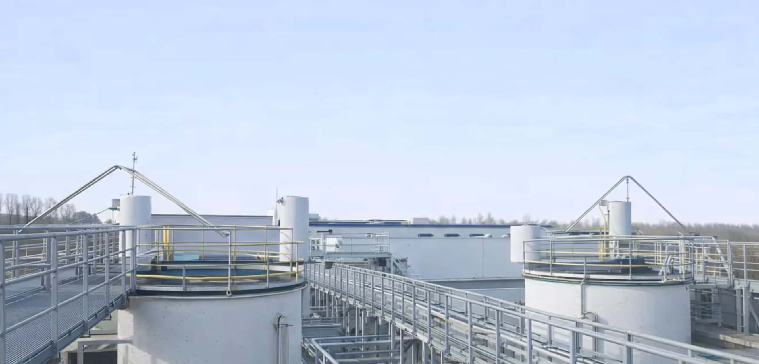 Two large circular industrial tanks connected by metal walkways and railings under a clear sky.