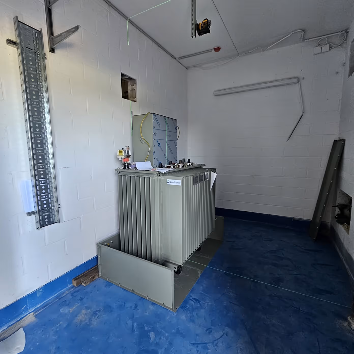 Industrial electrical transformer installed on blue floor inside white-walled room.