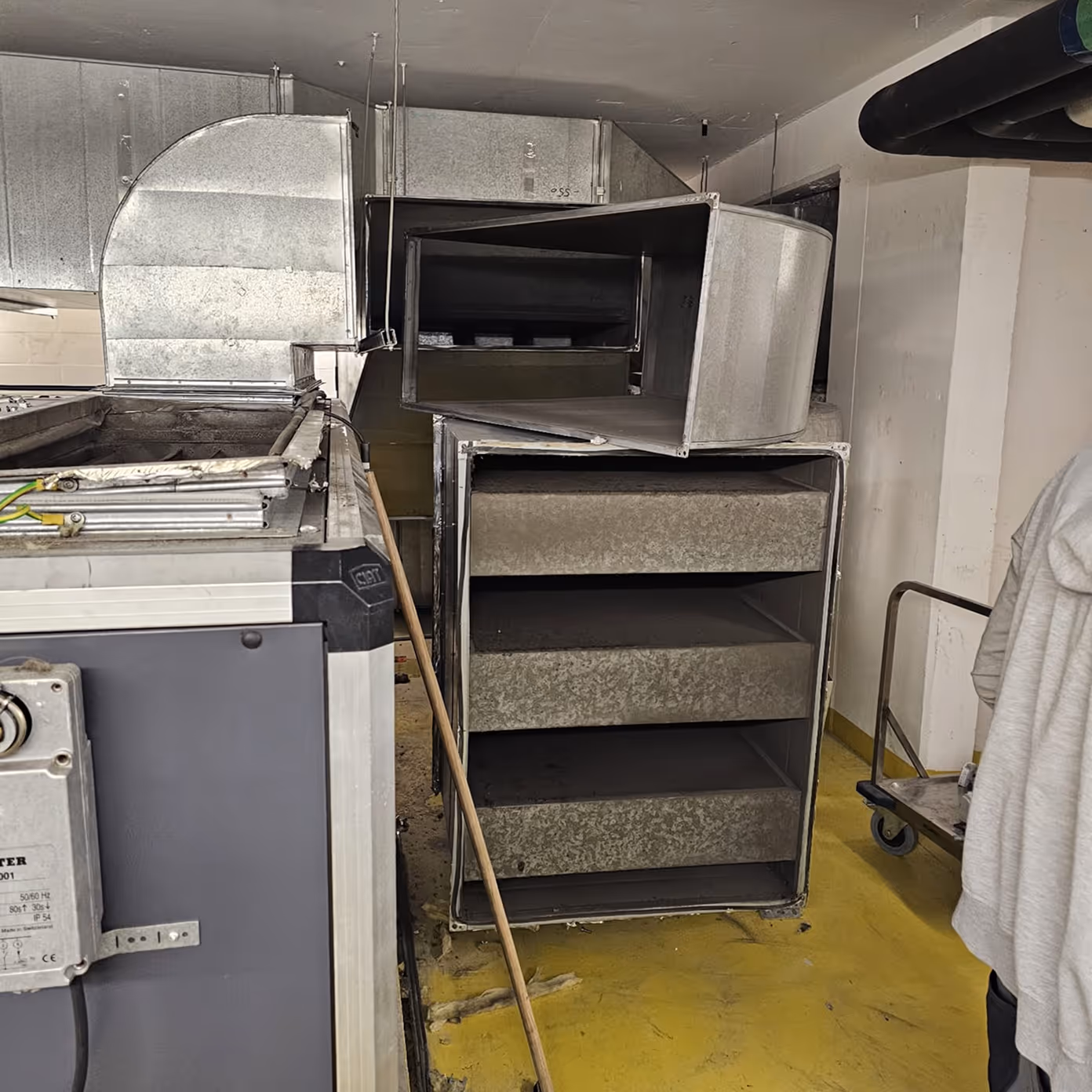 Large industrial metal HVAC ducts and ventilation equipment in a yellow-floored utility room.