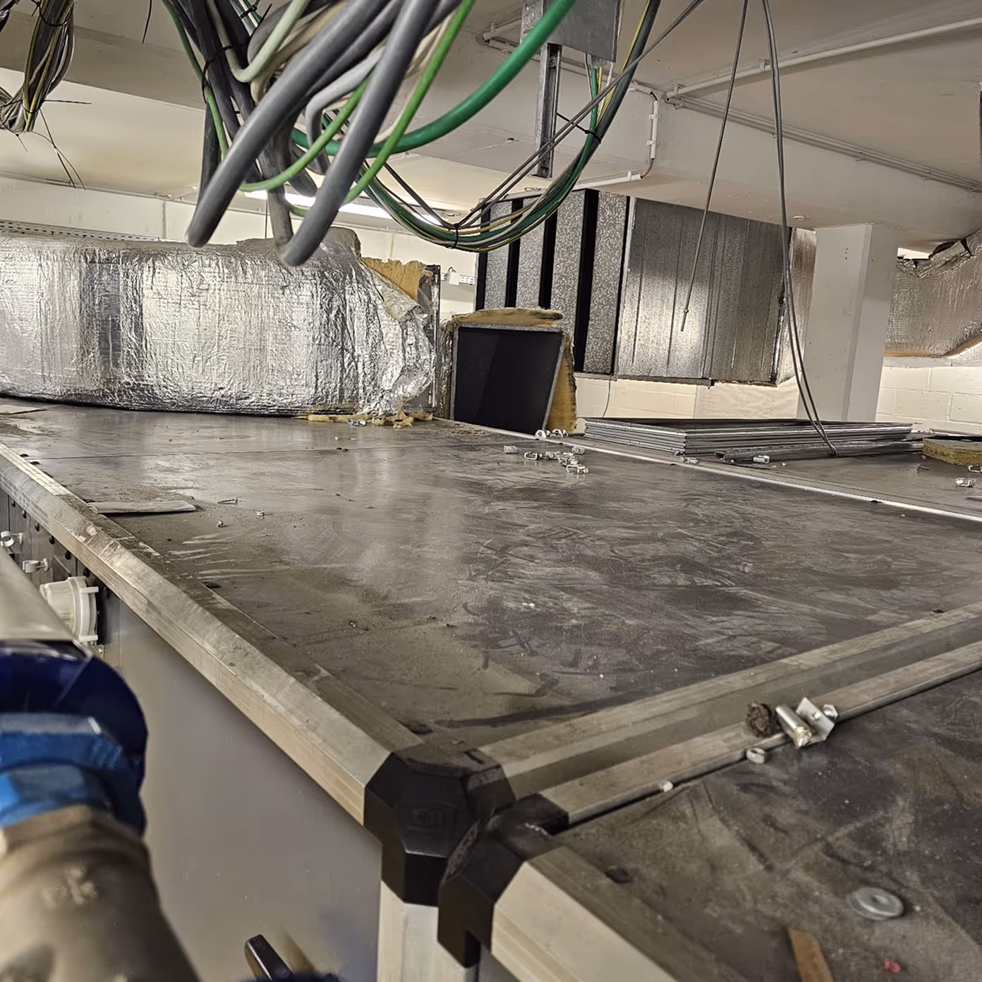 Dusty metal surface with screws, insulation, and hanging green and black wires in an industrial setting.