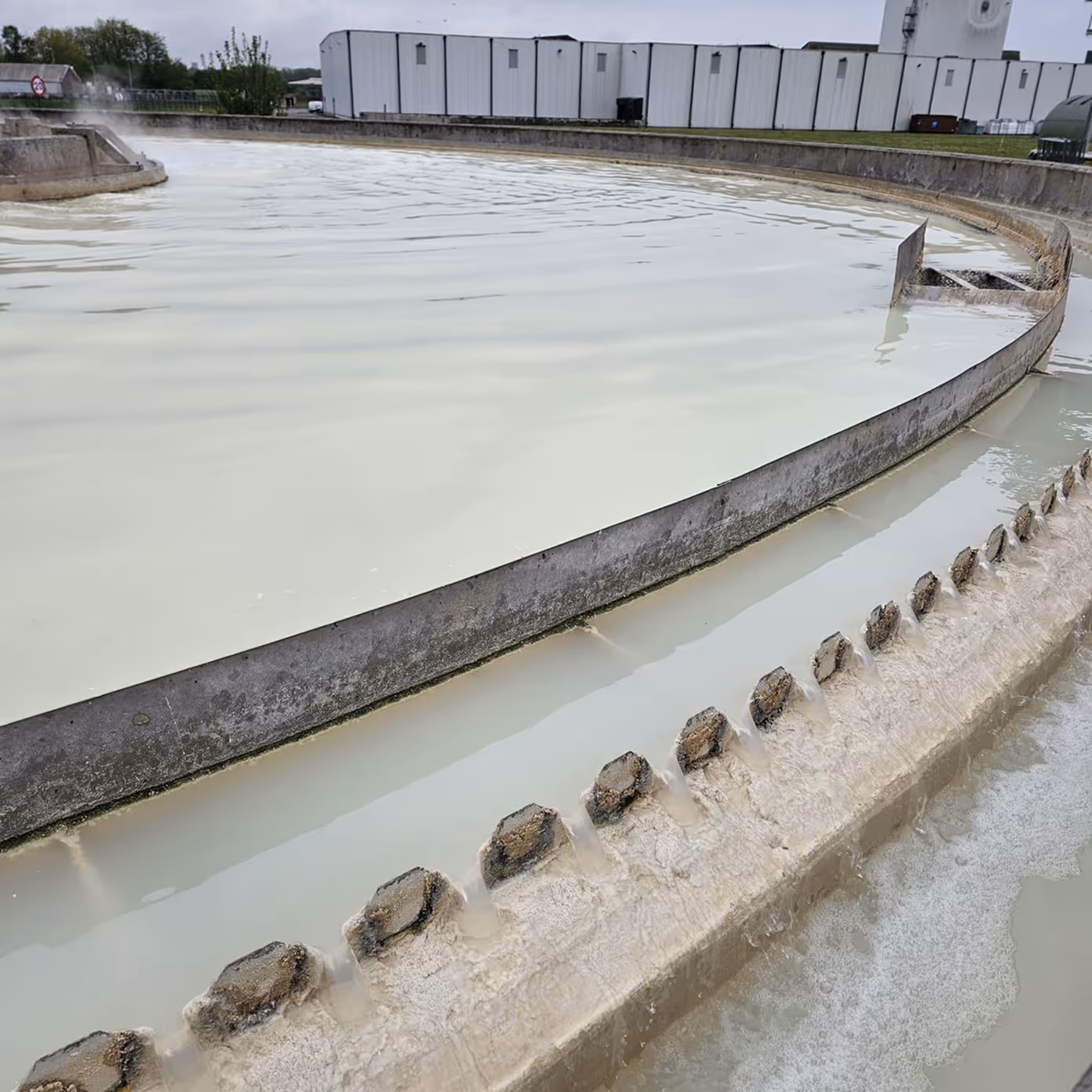Close-up of a water treatment plant's circular sedimentation basin with flowing milky water.