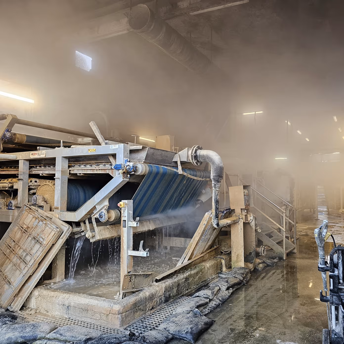 Industrial machine with conveyor belt processing material inside a misty, wet factory area.