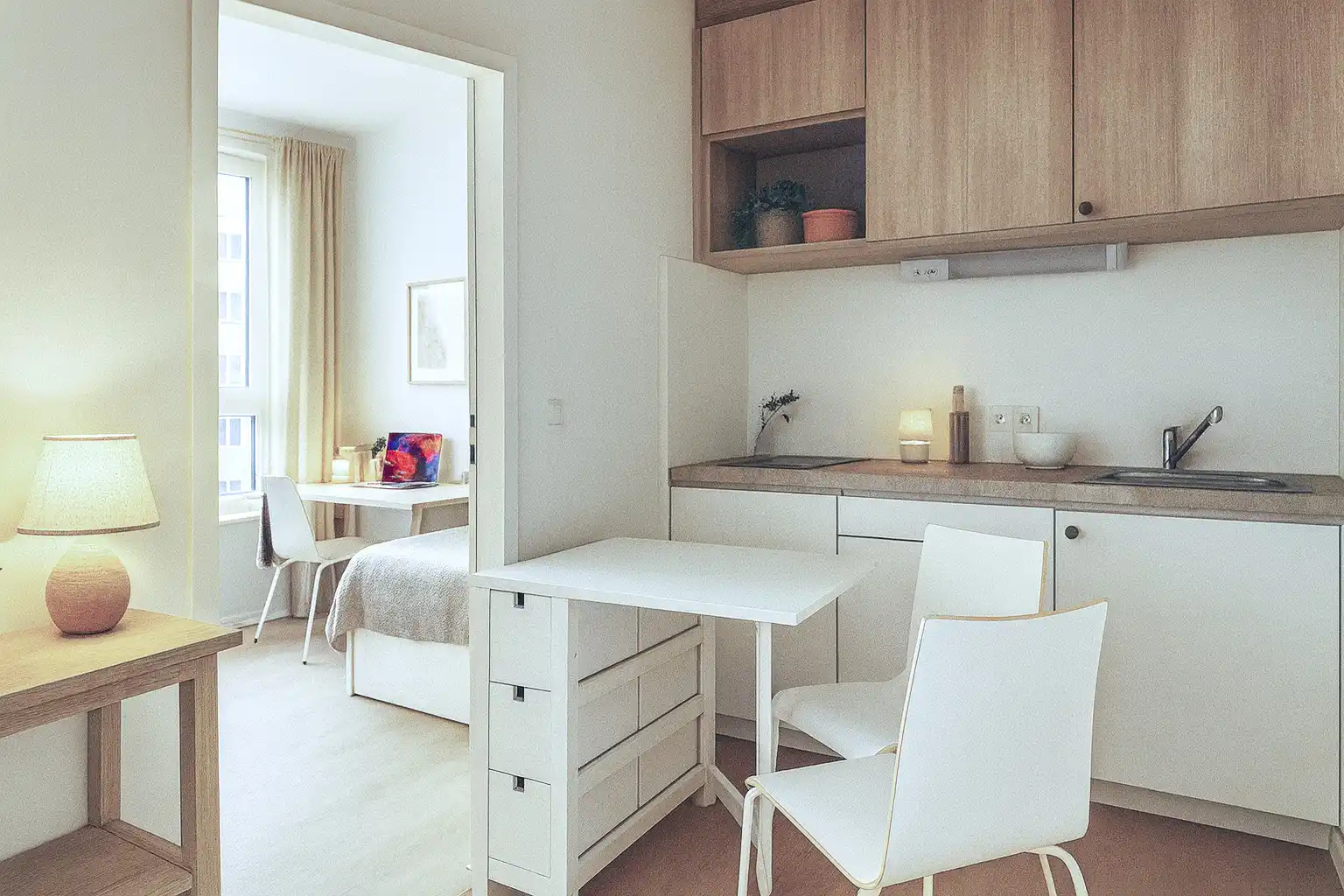 Kleine moderne Küche mit Tisch, Stühlen und Blick in ein Zimmer mit Schreibtisch und Bett im Holzmarkt 51 Gebäude.