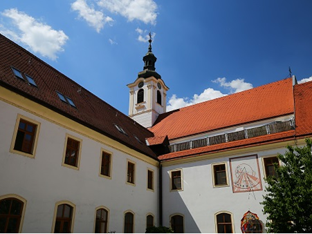 Historic building with red-tiled roofs and a tower under a blue sky with scattered clouds.