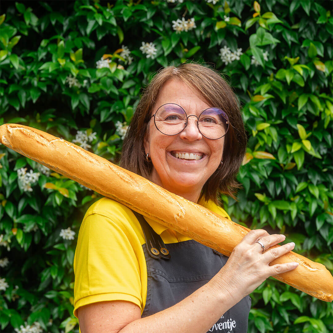 Foto van Marianne met een stokbrood op haar schouder. Verkoopster bij bakkerij 't Oventje