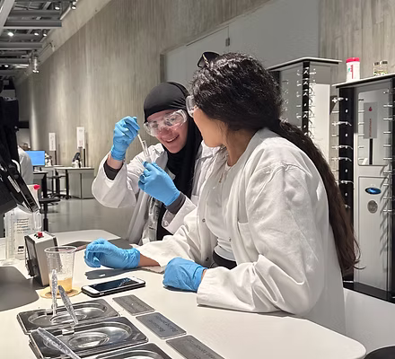 Zwei weibliche Wissenschaftlerinnen in Laborkitteln und Handschuhen arbeiten gemeinsam an einem Experiment.