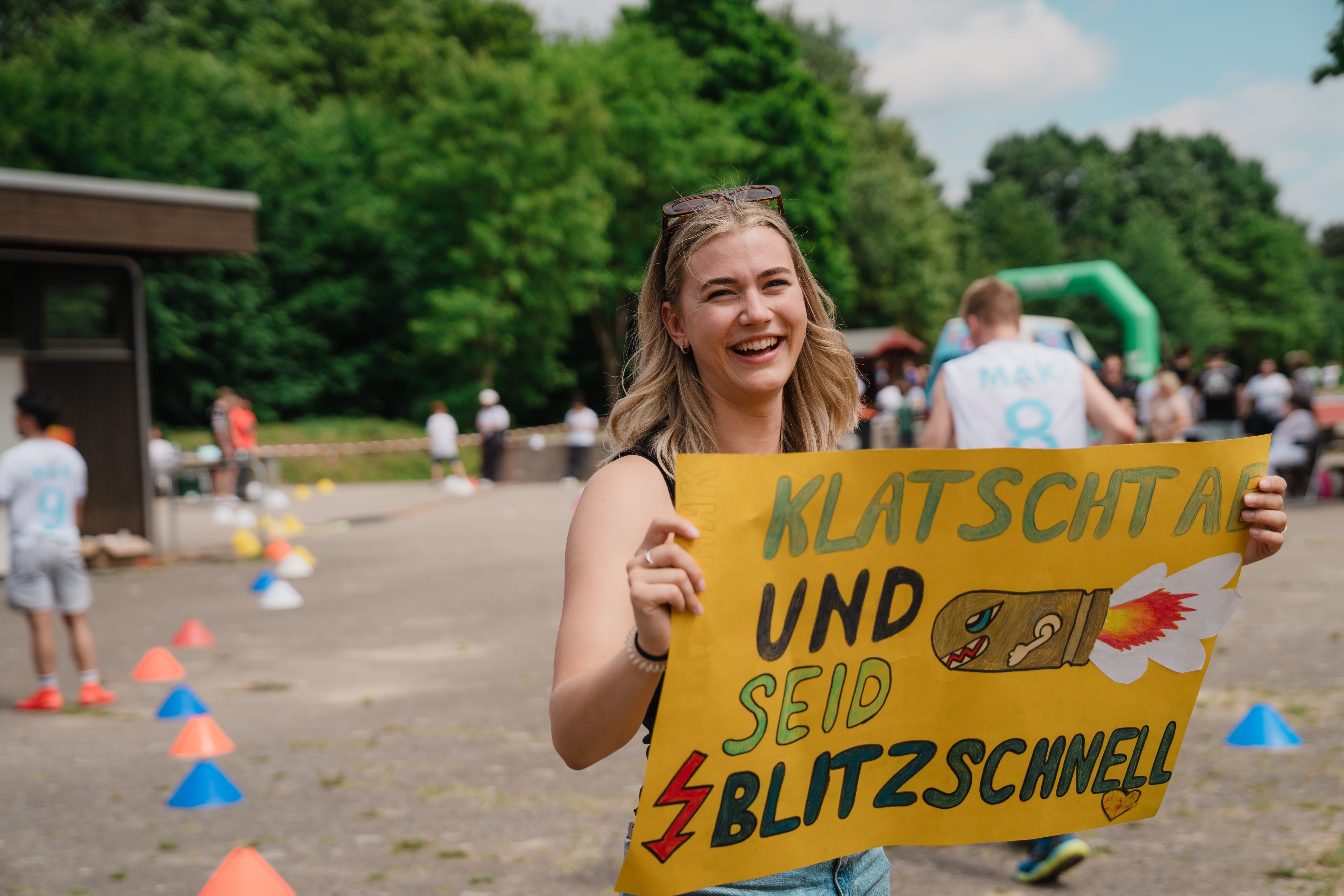 Lächelnde Frau hält ein gelbes Plakat mit der Aufschrift Klatscht ab und seid blitzschnell.