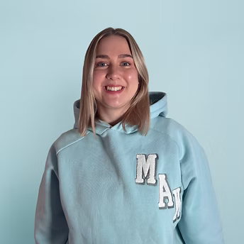 Frau mit blonden Haaren und hellblauem Kapuzenpullover vor hellblauem Hintergrund.
