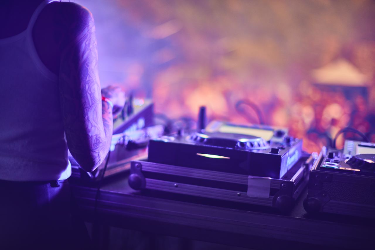 DJ con tatuaggi usa attrezzatura da mixer in un ambiente illuminato con luci viola.