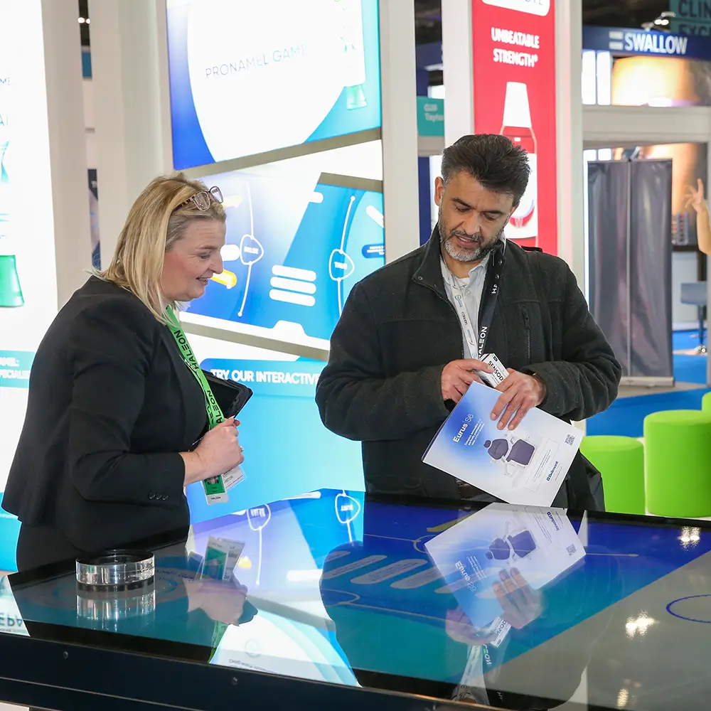 Two people discussing a brochure over an interactive digital table at a trade show booth.