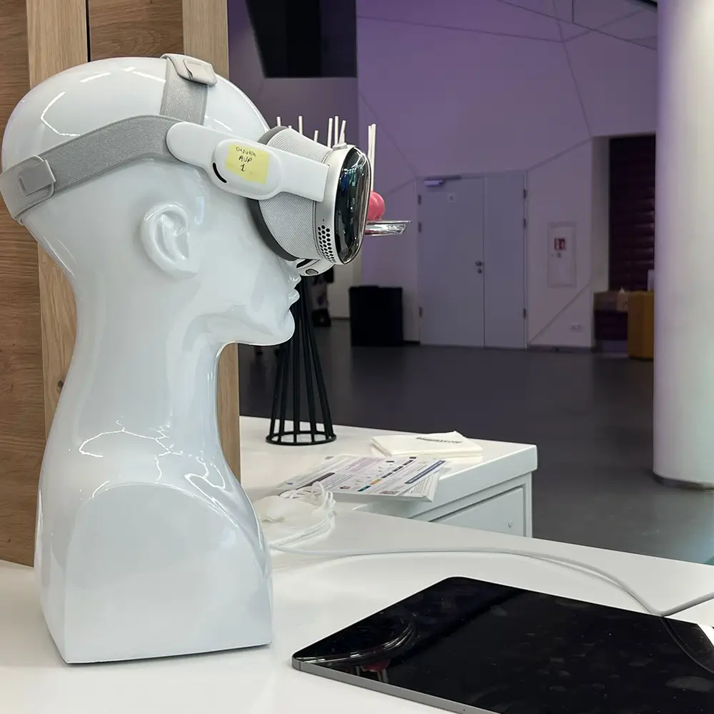 White mannequin head wearing a VR headset on a white table with a tablet and charger cable.