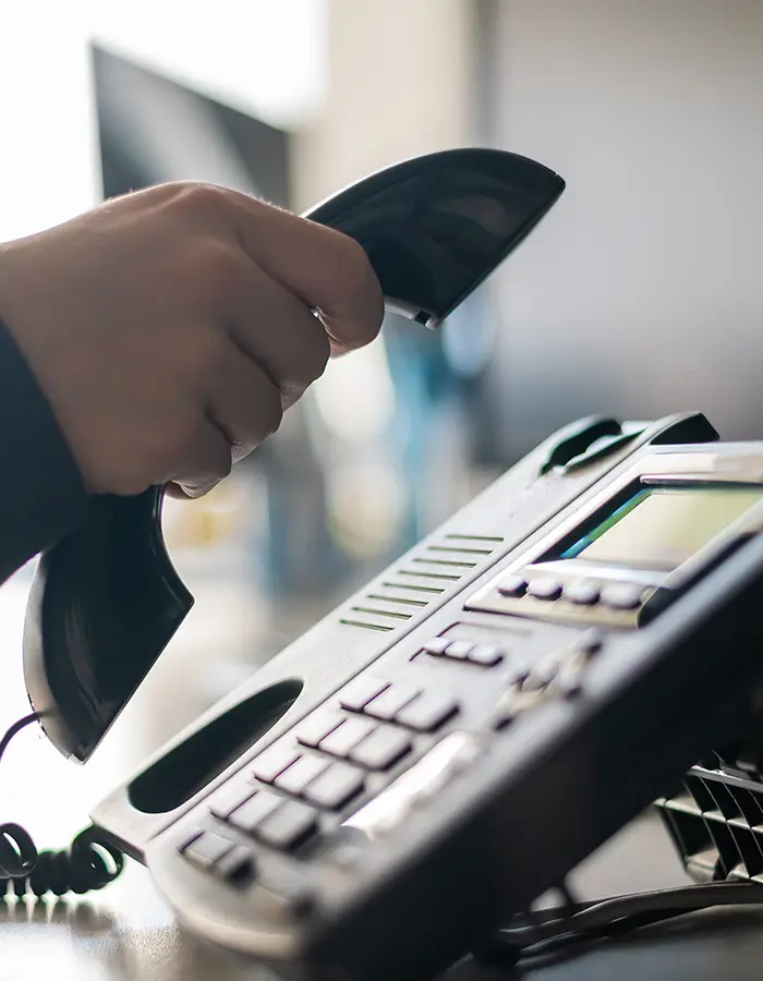 Person lifting a black office phone handset from its base on a desk.