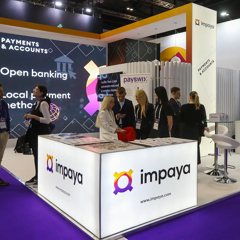 Impaya booth at a trade show with staff talking and promotional displays about payments and banking.