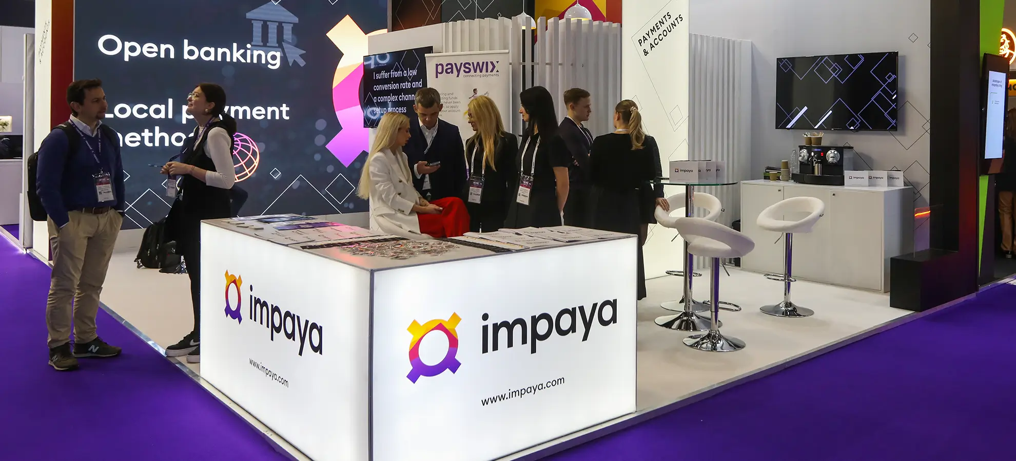 People gathered at an Impaya booth with open banking and payment displays at a trade show.