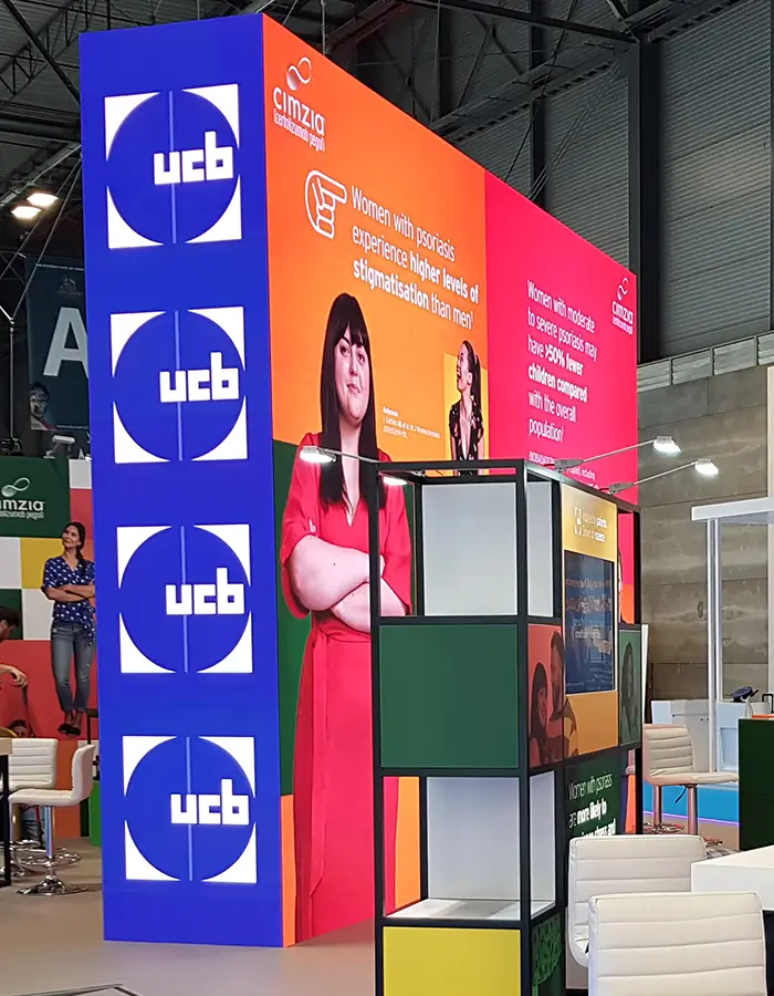 Exhibition booth with UCB logos and colorful panels highlighting psoriasis stigma, featuring a woman in red.