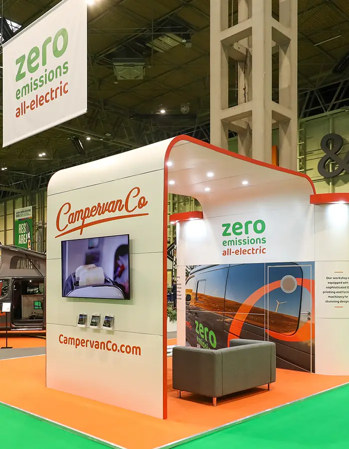 CampervanCo electric camper van exhibit with zero emissions signage and a gray couch on an orange floor.