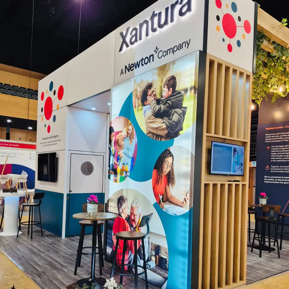Xantura booth display with images of diverse people and wooden stools with flower pots at an event.