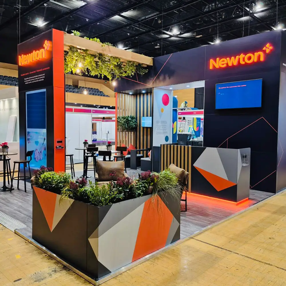 Modern Newton booth with geometric planters, seating area, and illuminated brand signs at event.