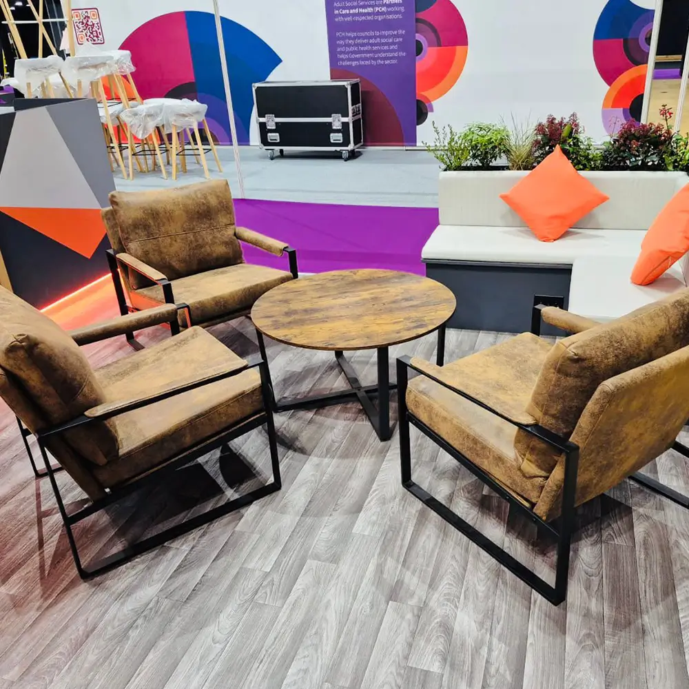 Three brown cushioned armchairs around a round wooden table on a wood floor with a white couch nearby.