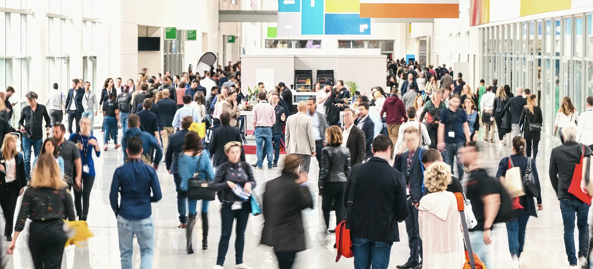 Crowded indoor hallway with many people walking and socializing near event booths.