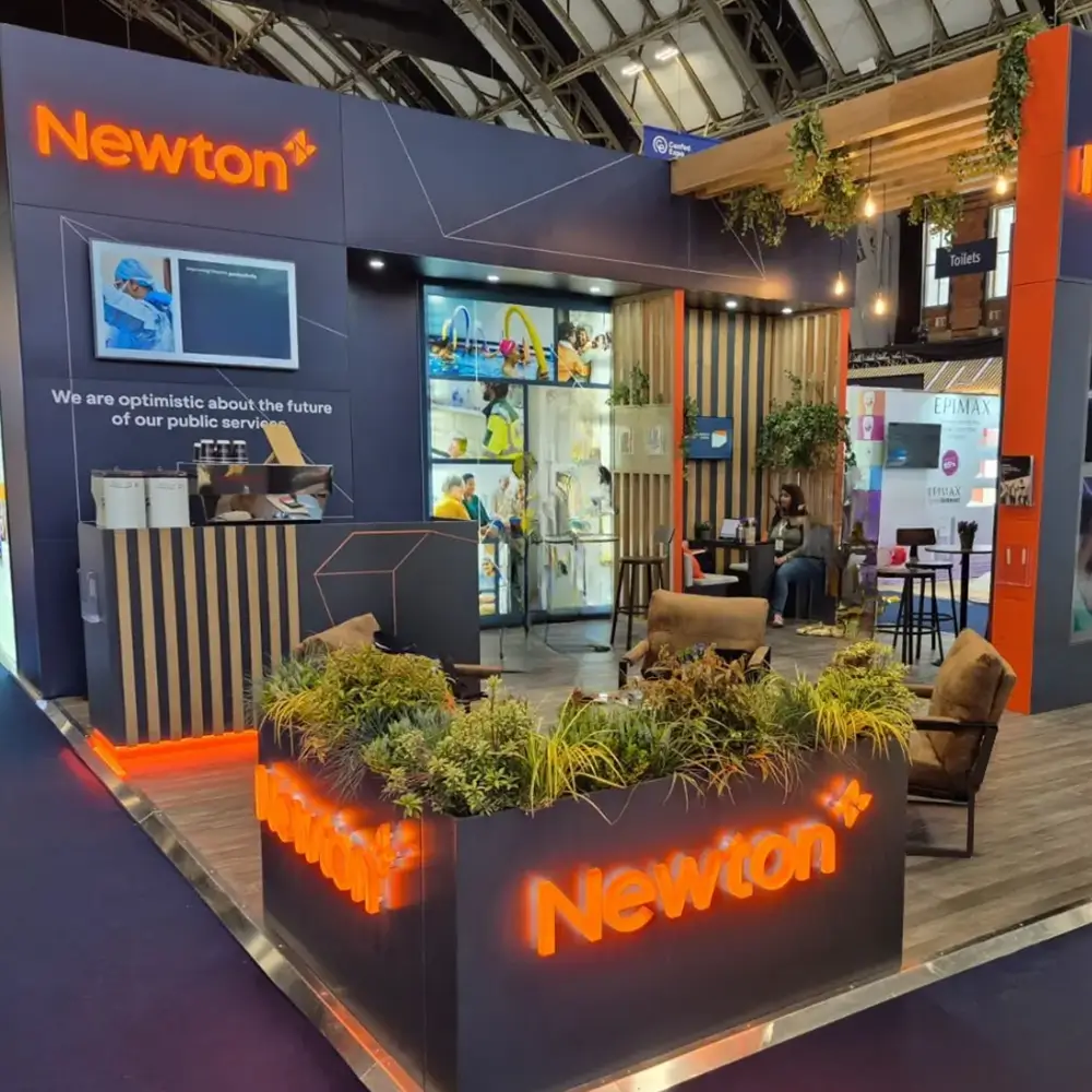 Newton booth at event with illuminated signs, seating area, plants, and people inside.